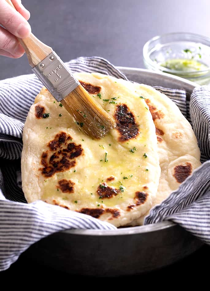 A person brushing cooked naan bread with a brush