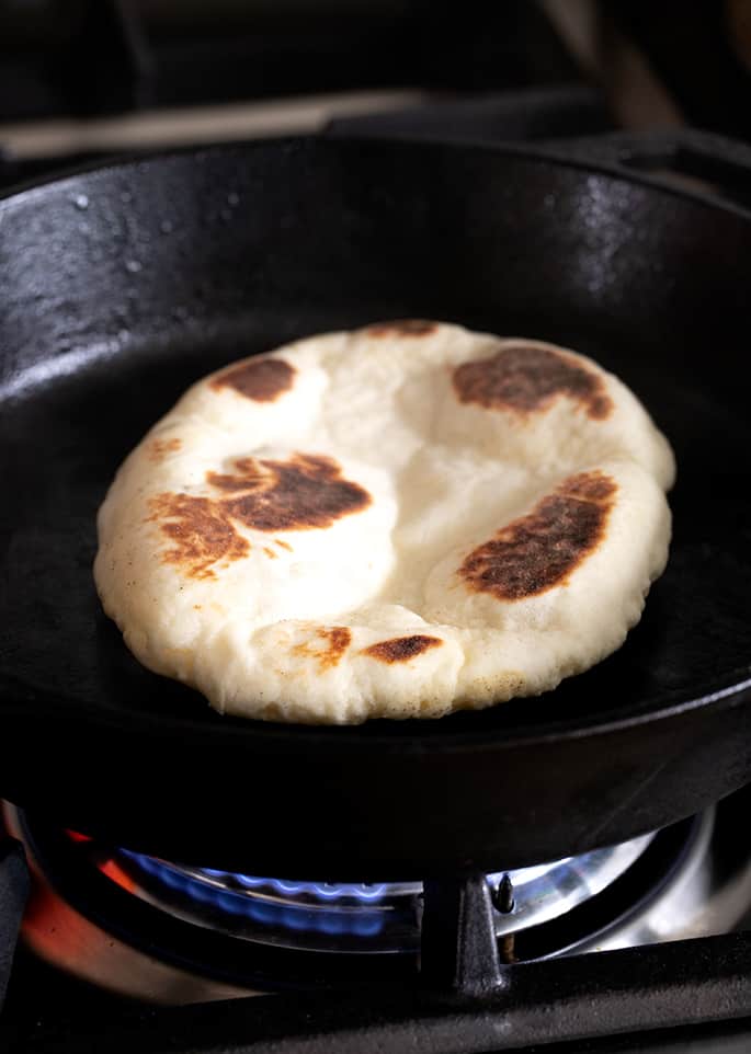 A cast iron skillet with cooking naan bread