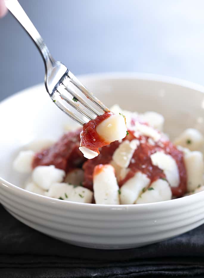 a light tan dumpling with tomato sauce on the tines of a fork