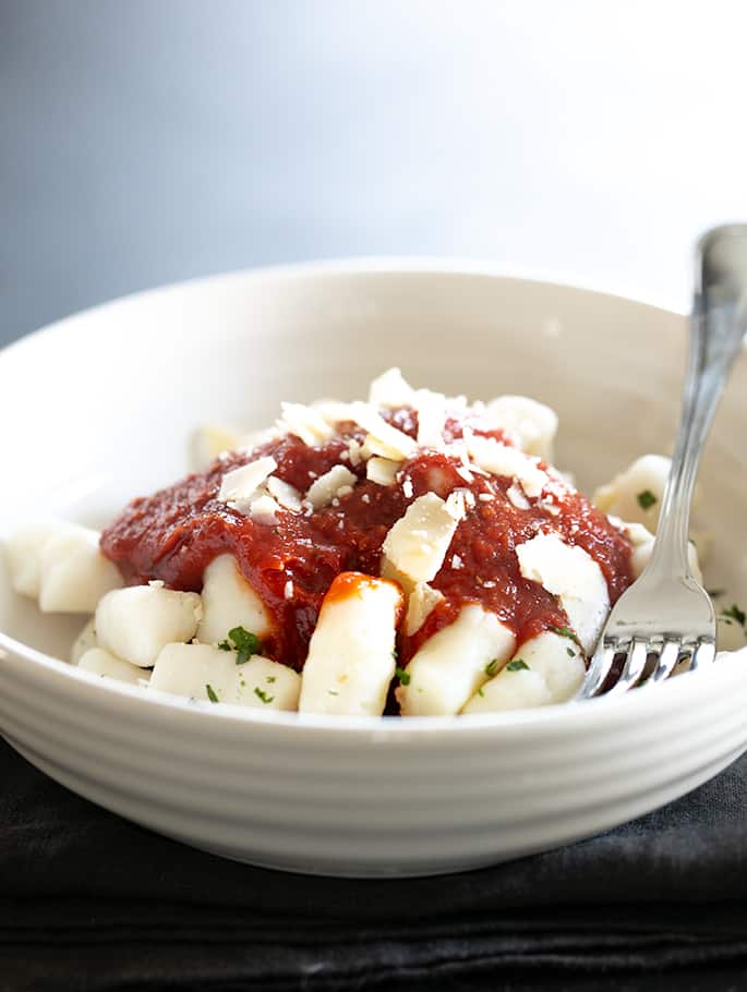 light ceramic bowl with gluten free gnocchi, tomato sauce, and a fork