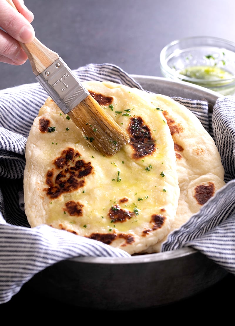 Gluten free naan bread wrapped in blue striped towels with pastry brush