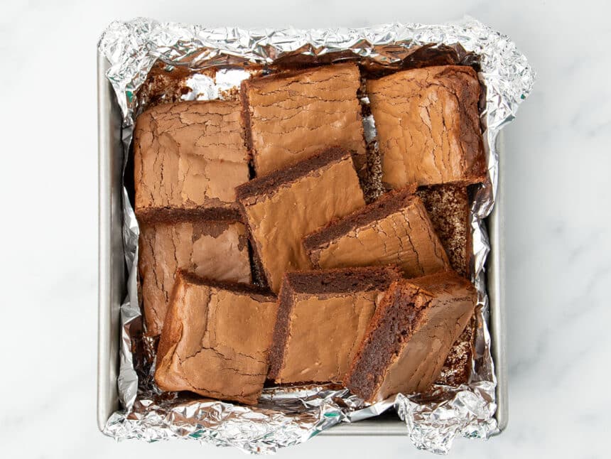 9 cut square brown 3 ingredient brownies in same pan with tops and darker brown sides of brownies visible