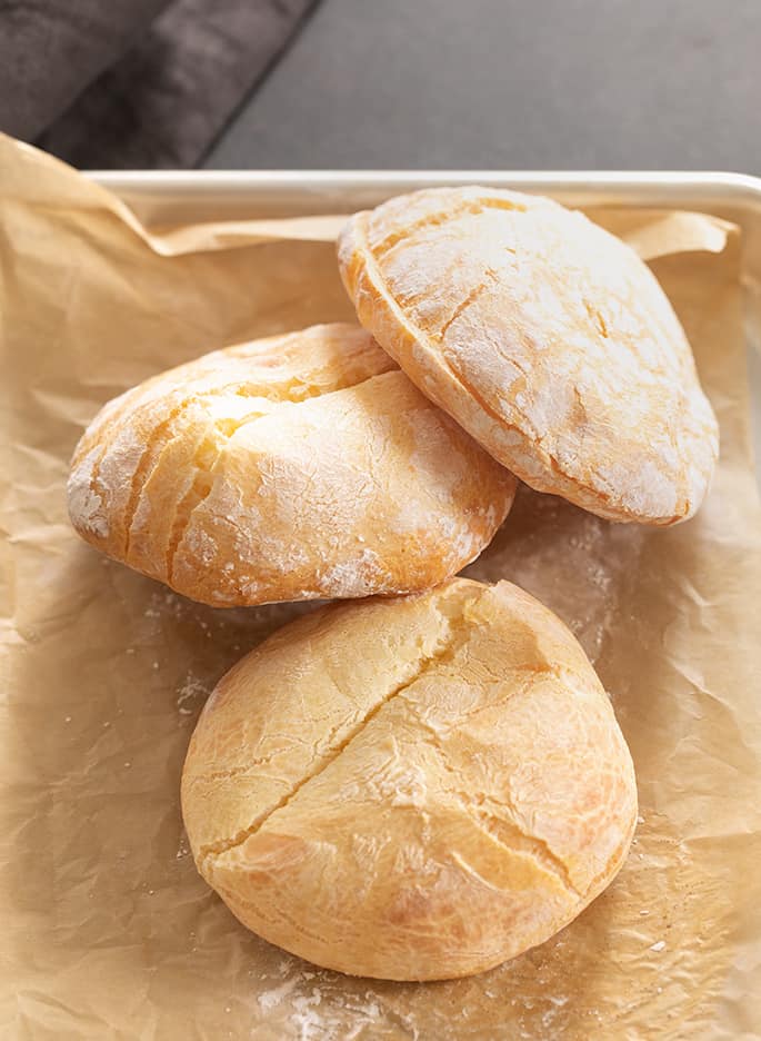 3 pale brown sliced rolls piled on top of one another on brown crinkled paper