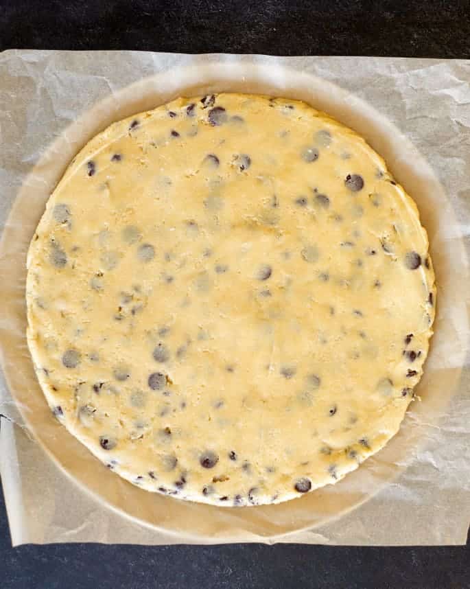 overhead image of raw light brown cookie dough with dark chocolate chips in large round flat shape