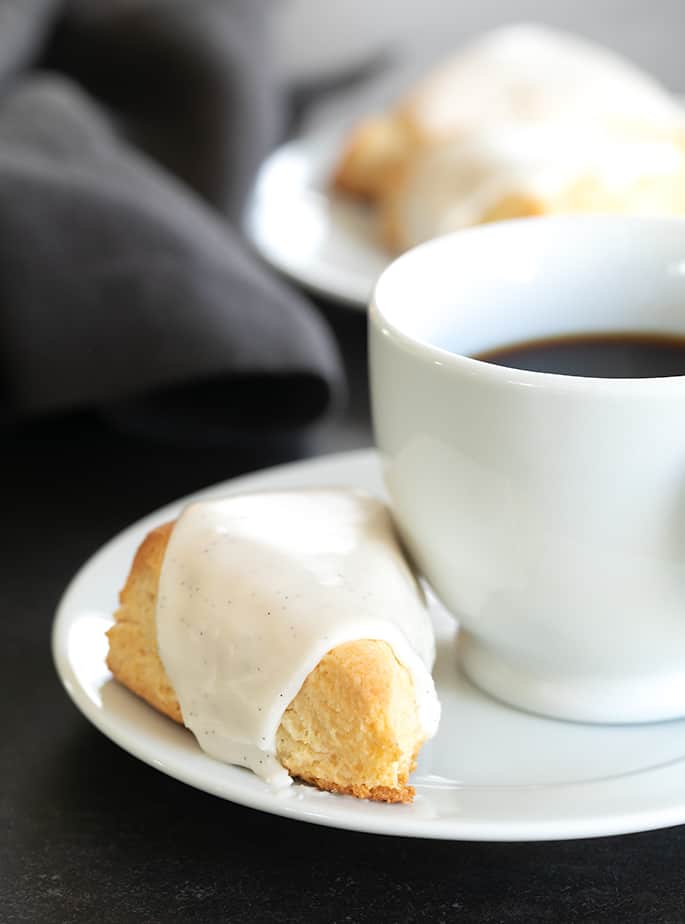 A close up of an iced vanilla scone with a cup of coffee on a plate