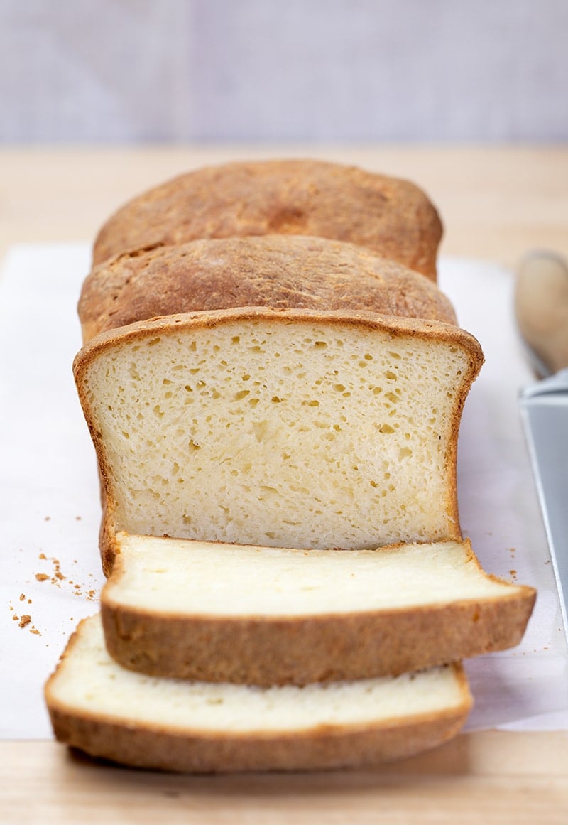 Loaf of breaad with 2 slices on white paper with a large bread knife