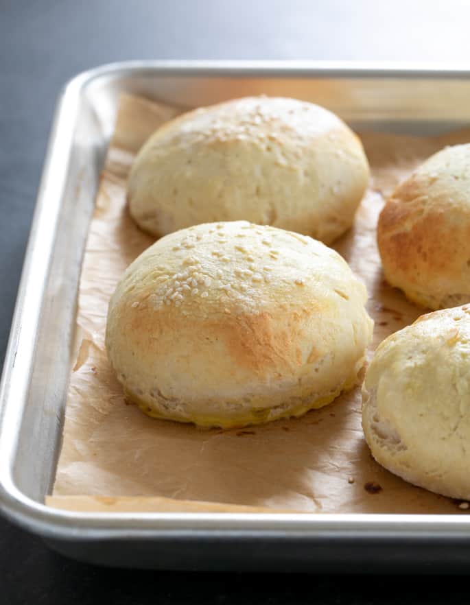 Baked round light brown bread buns on brown paper on baking sheet