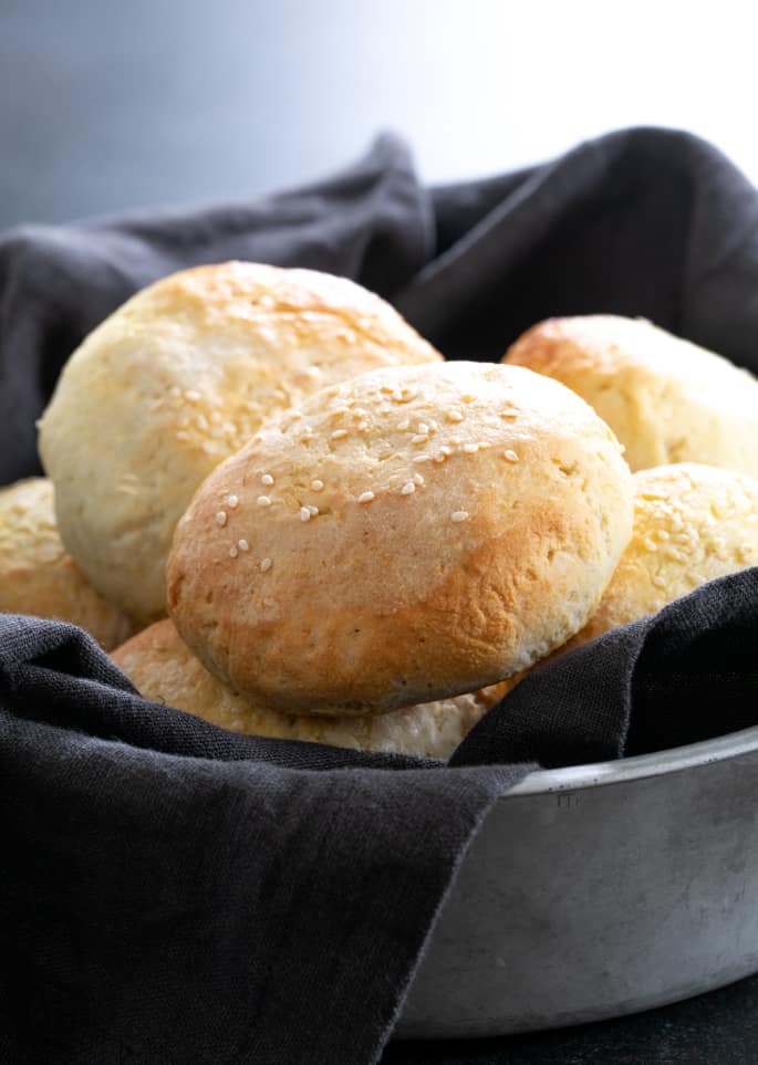 Round hamburger buns with sesame seeds on top in a pile in a dark gray cloth