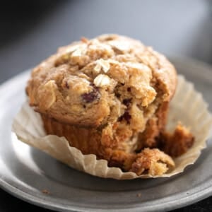 gluten free morning glory muffin in liner on gray small plate with one bite taken