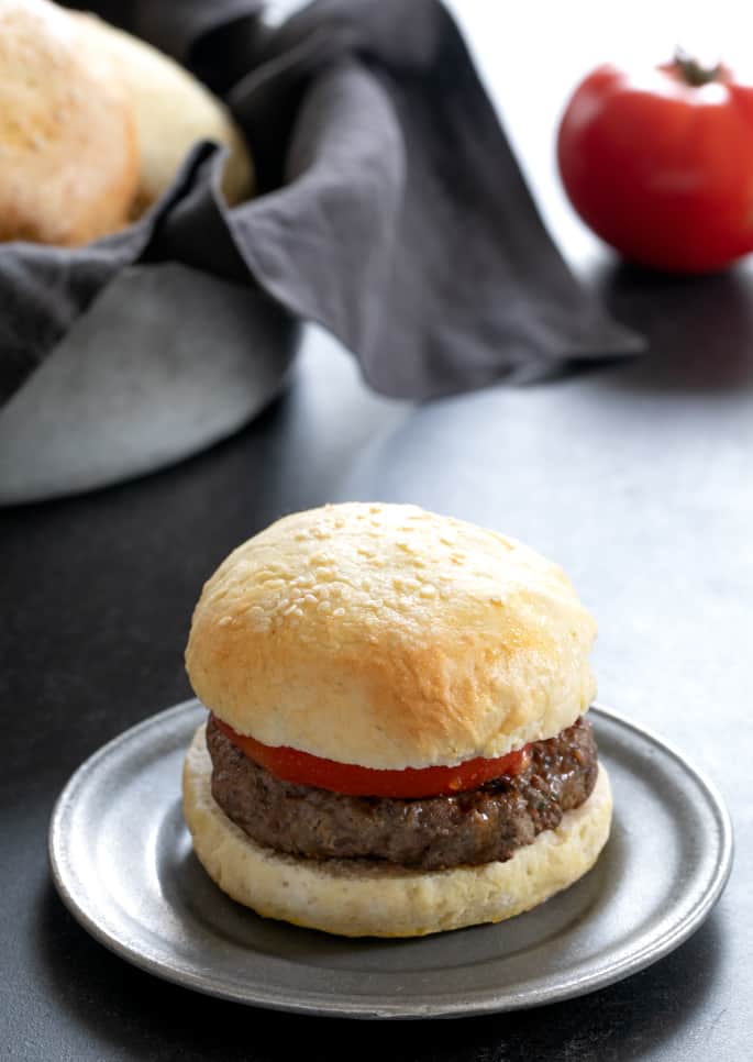 light brown round bun with sesame seeds split in half with hamburger and tomato slice in between