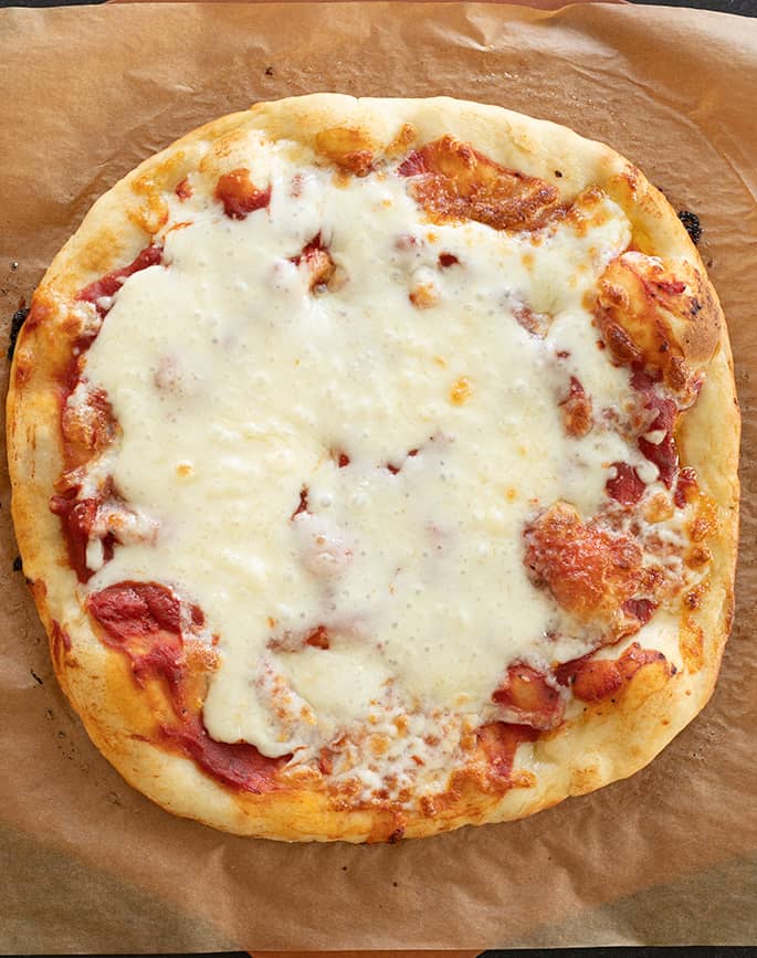 Overhead image of whole baked gluten free pizza with sauce and cheese