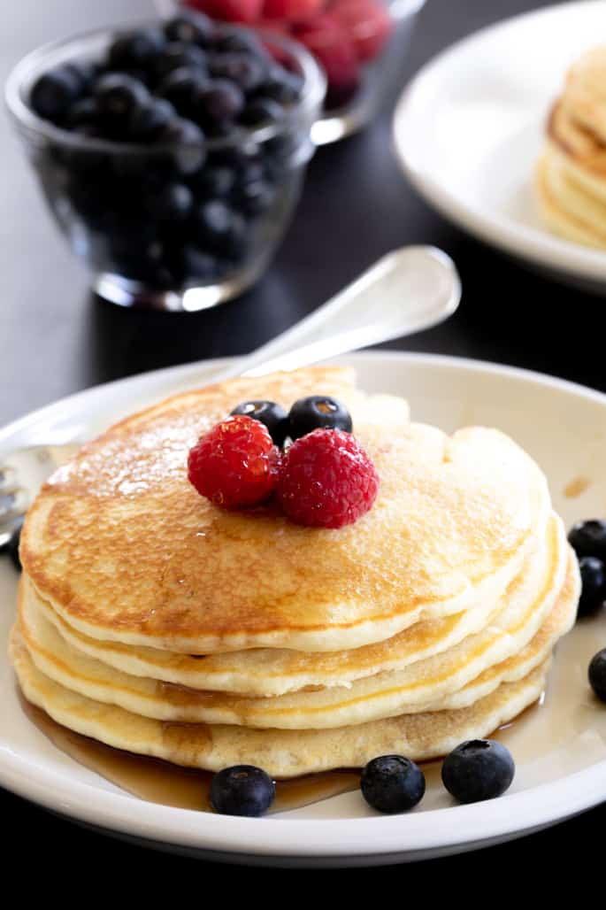 A stack of gluten free pancakes on a plate with a fork and berries