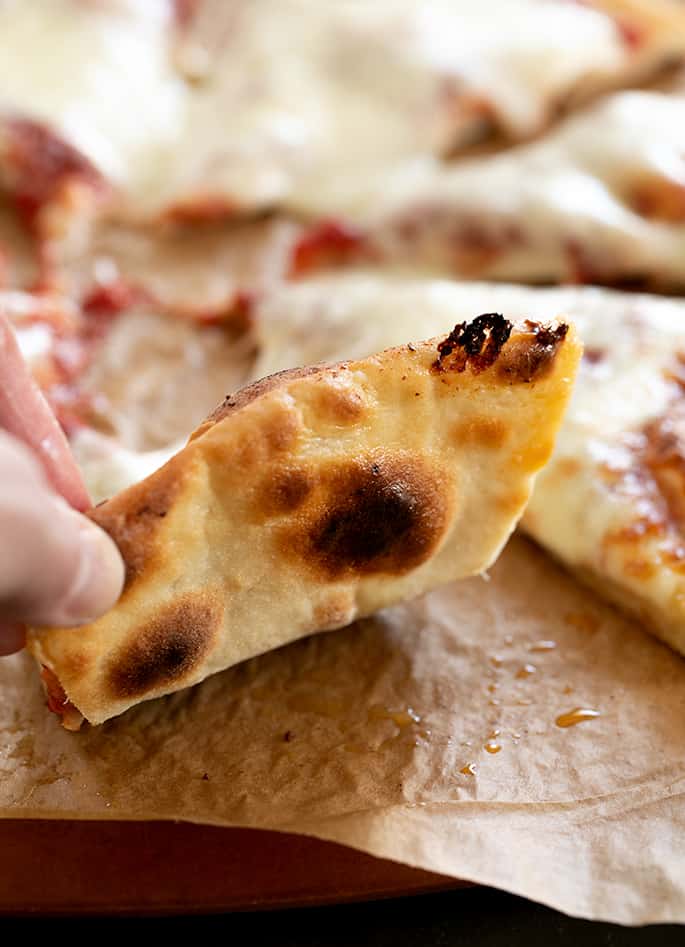 A slice of gluten free pizza sitting on top of a wooden cutting board, being picked up to show underside