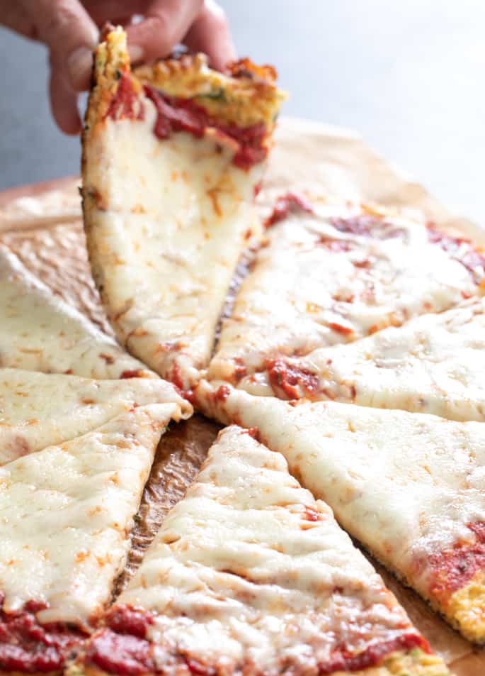 Image of a zucchini keto pizza with a hand taking a slice