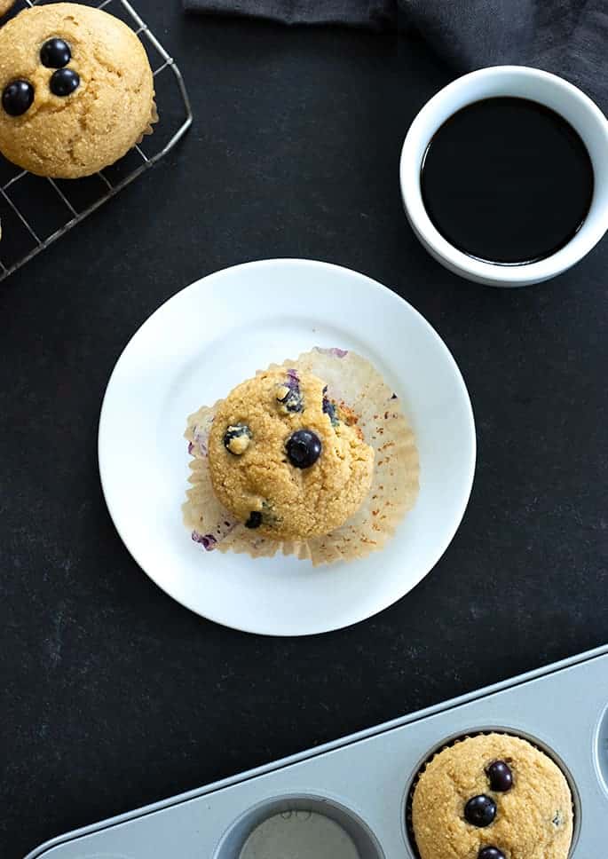 A plate with a cup of coffee, with a blueberry muffin overhead