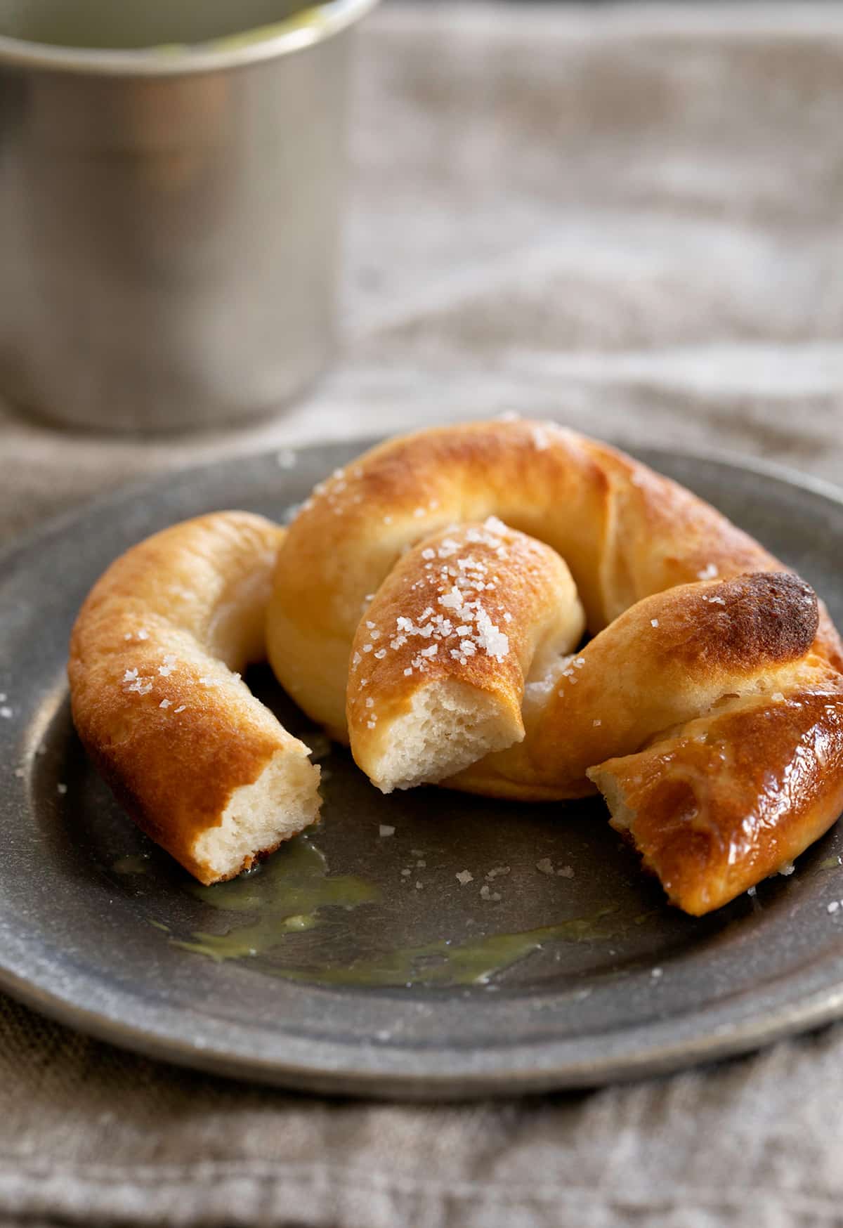 A partially eaten gluten free soft pretzel on a plate with dipping sauce.