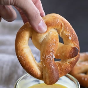 gluten free soft pretzels in fingers about to be dipped in yellow honey mustard sauce