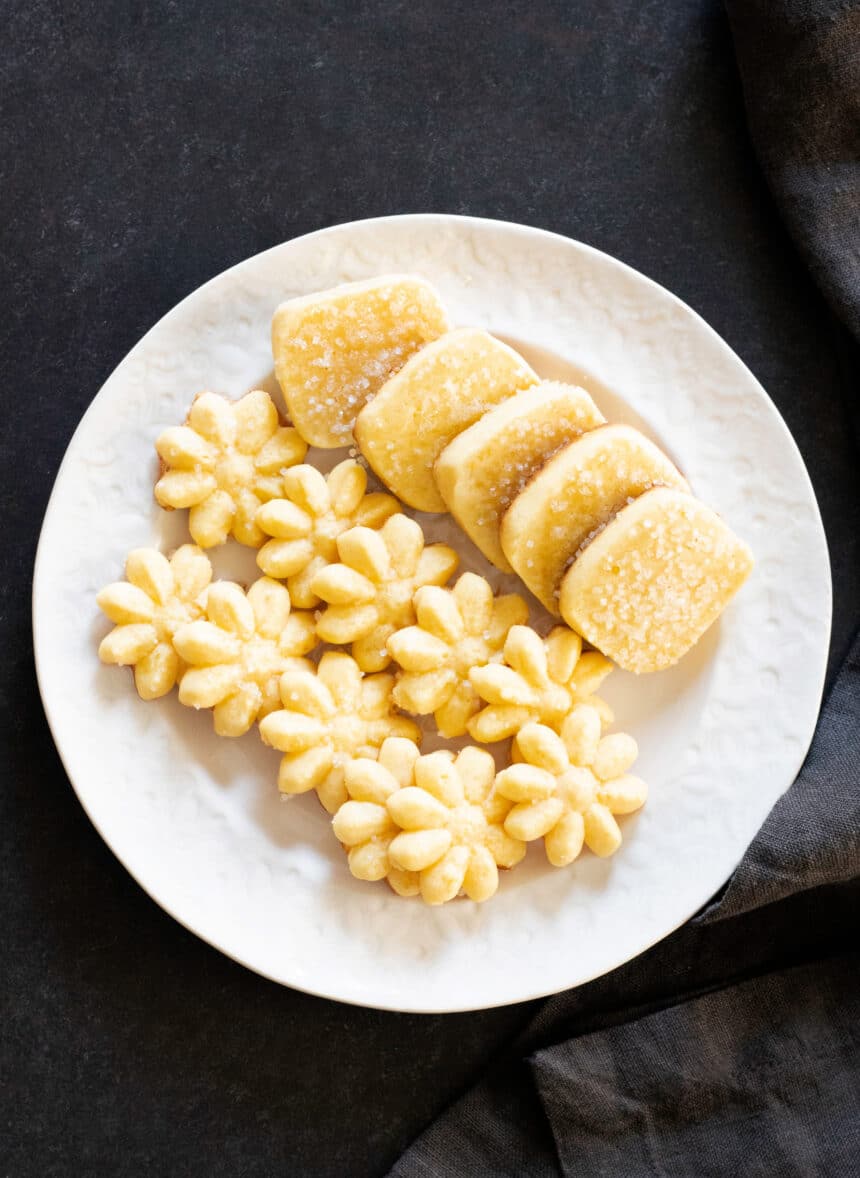 overhead view of round white plate with 2 rows of spritz flower shaped butter cookies and one row of rectangular butter cookies