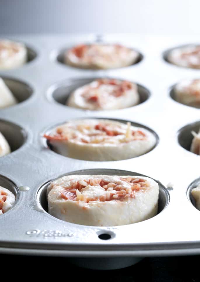 Gluten free pizza pinwheels pictured raw in muffin tin wells.