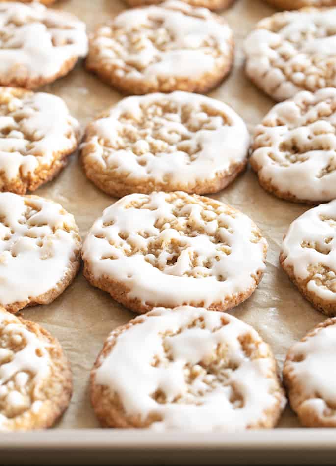 Thin and chewy gluten free oatmeal cookies with light icing on top on a baking tray