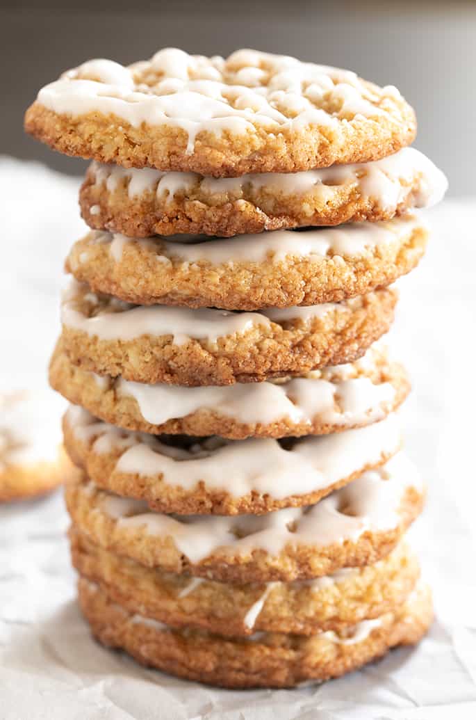 Tall stack of iced thin and chewy gluten free oatmeal cookies.