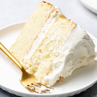 Small image of gluten free vanilla layer cake with white vanilla frosting on a small white plate with a gold colored fork