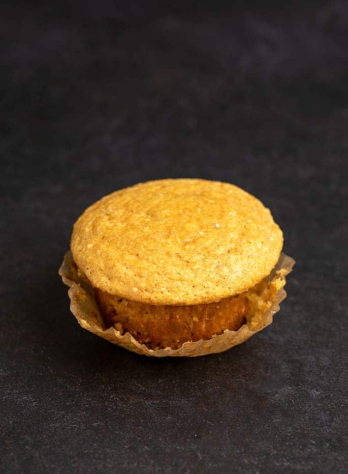 Image of single corn muffin on black surface with brown muffin wrapper pulled down partially