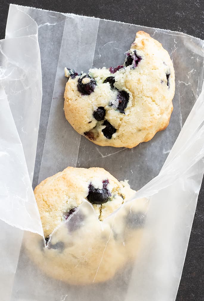 overhead image of pale brown round baked goods with blueberries in a wax paper bag