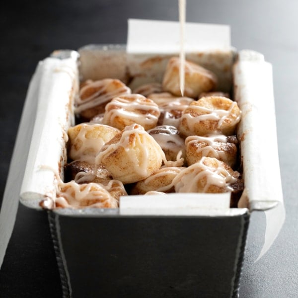 closeup of baked cinnamon sugar gluten free monkey bread in metal loaf pan being drizzled with sugar glaze
