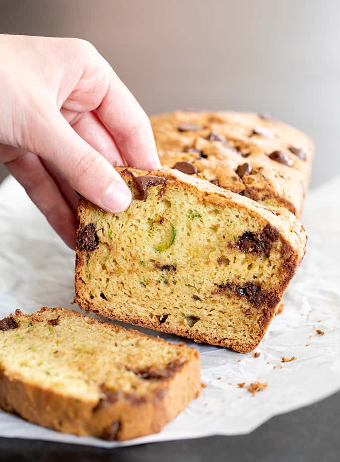 Slice of light brown gluten free zucchini bread with chocolate chips and green flecks being grabbed by fingers