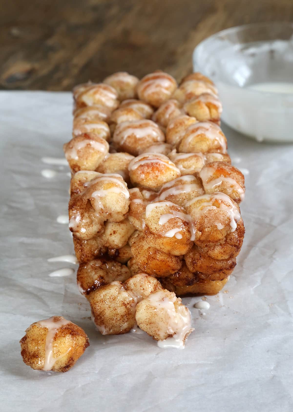 Whole loaf of monkey bread on white paper with a few pieces falling off loaf showing soft, cinnamon sugar covered center