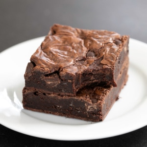 stack of two flourless brownies one with a bite taken from the corner both on a small white plate on a black surface