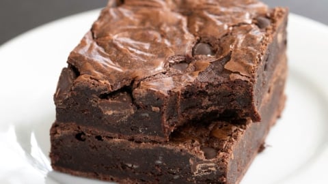 stack of two flourless brownies one with a bite taken from the corner both on a small white plate on a black surface