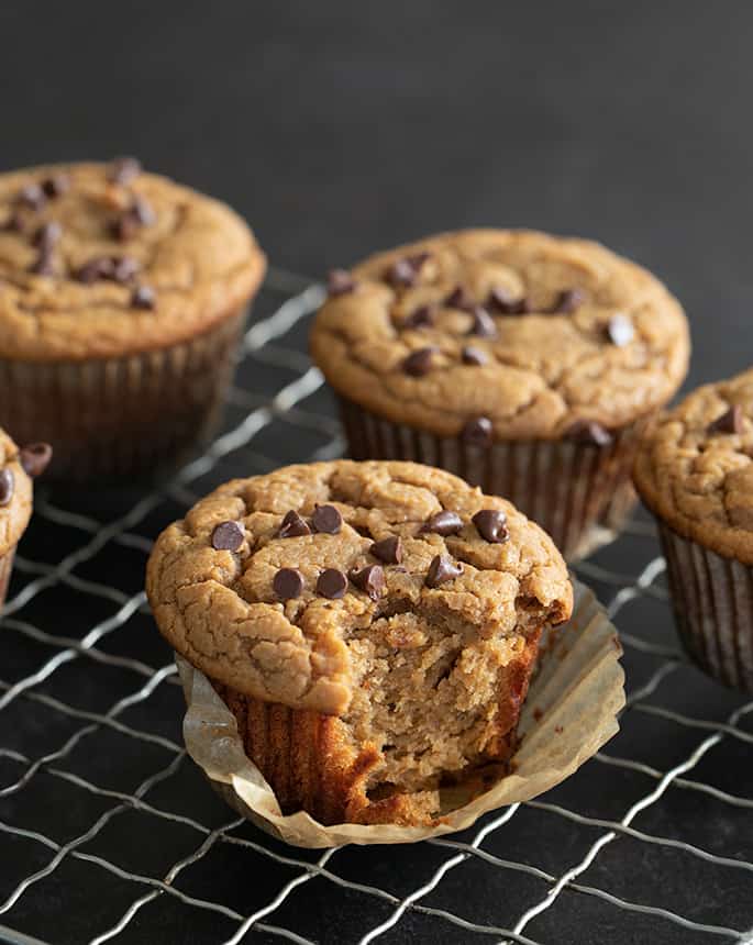 Flourless peanut butter muffins on a wire rack, one with a bite taken.