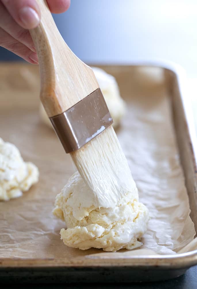 Brushing raw gluten free cream biscuits with cream before putting them in the oven.