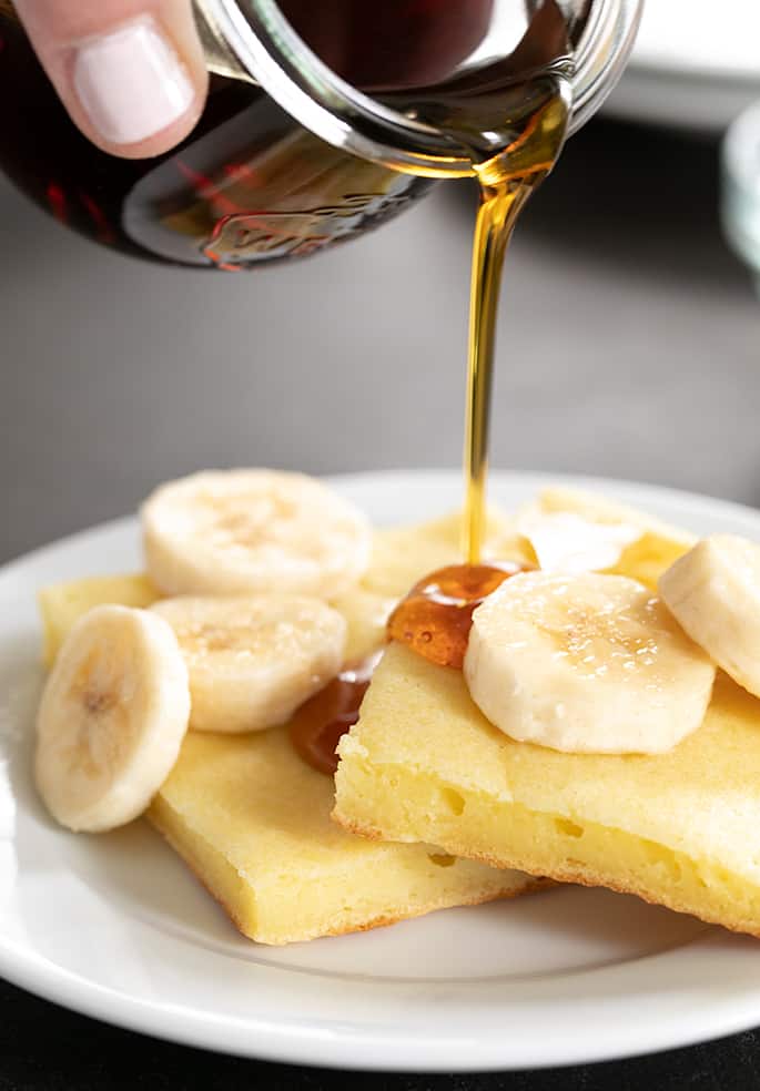 A close up of a plate of sheet pan pancakes with bananas and syrup