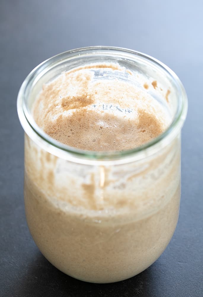 Active and bubbling light brown sourdough starter in glass jar.