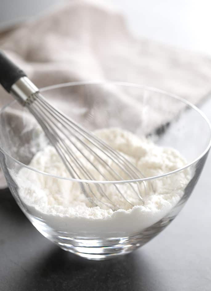 A glass bowl containing gluten free bread flour with a whisk resting in it