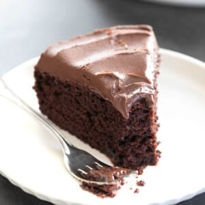 slice of gluten free chocolate cake with chocolate icing with fork on small white plate