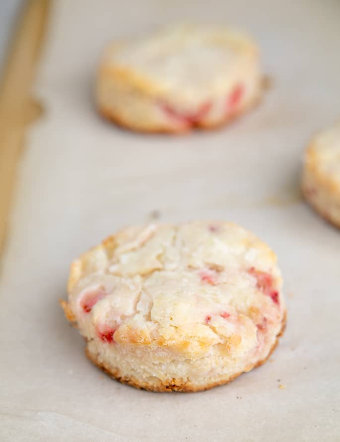 3 baked strawberry shortcake biscuits on white paper on tray