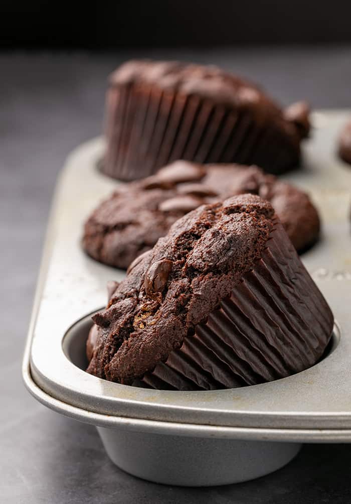 Baked chocolate muffins in metal tin with some on their sides