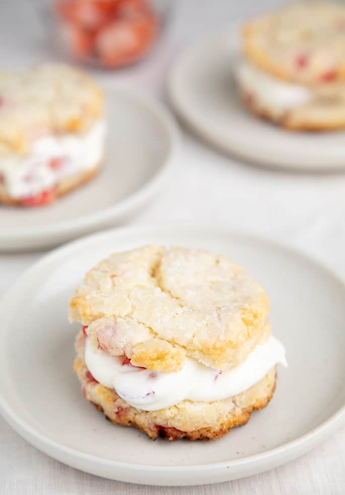 Strawberry shortcake biscuits with cream filling on small white plates image from side