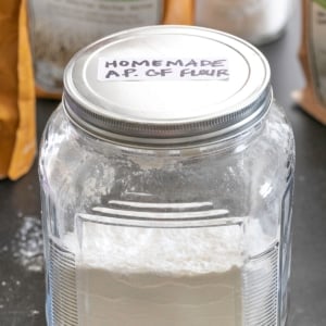 large glass jar with white flour inside and metal lid with white label stating homemade a.p. gf flour