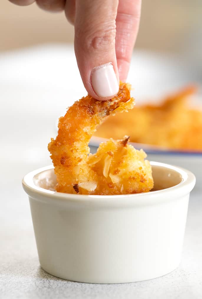 Coconut shrimp being dipped into small ramekin of sauce