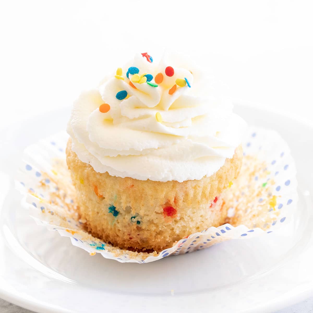 one gluten free funfetti cupcake partially unwrapped with white frosting with edible confetti on top