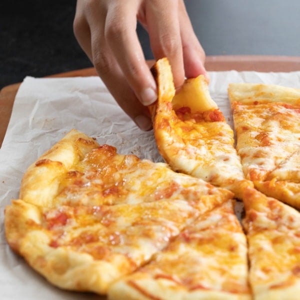 fingers picking up slice of NY style gluten free pizza crust