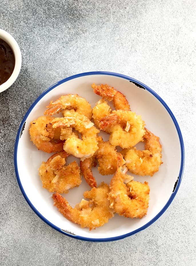 Overhead image of coconut shrimp on a white plate with dipping sauce next to the plate