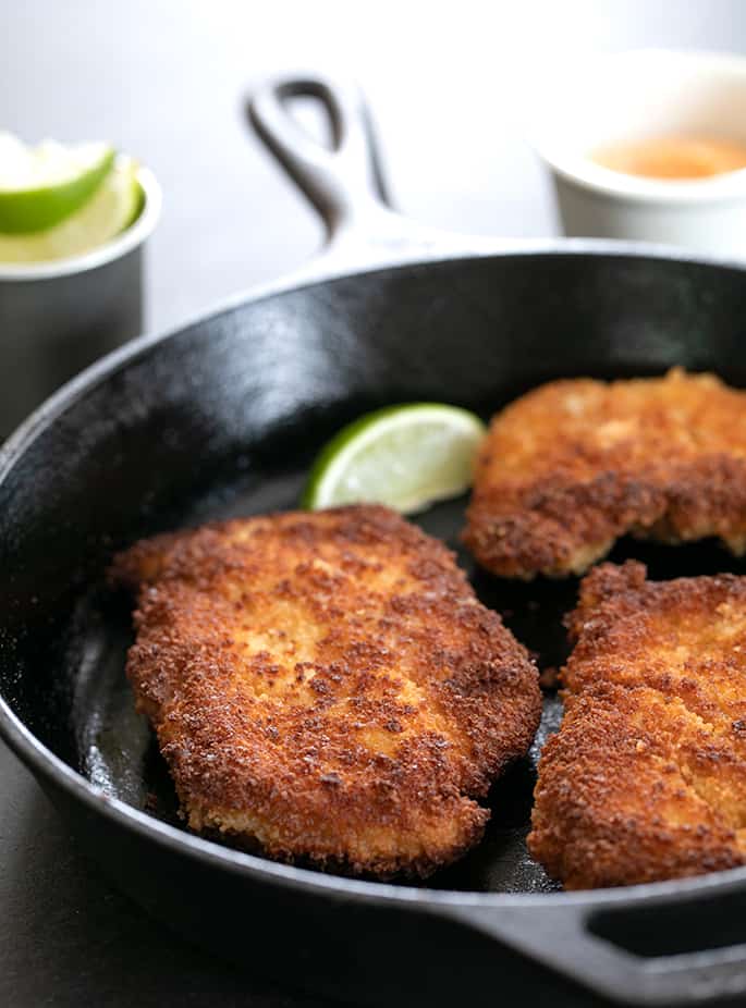 Spicy Chicken Cutlets in cast iron skillet with limes and dipping sauce