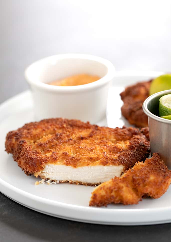 Spicy chicken cutlet on a plate with limes and dipping sauce