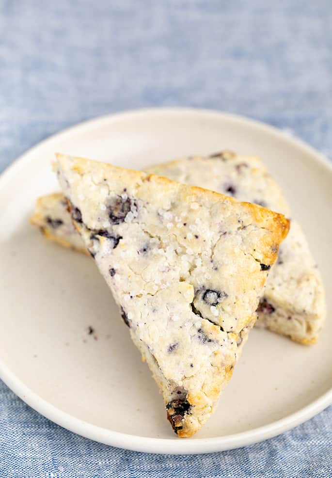 2 blueberry lemon scones on small white plate on blue cloth